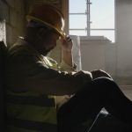 overworked tired safety professional sitting on ground with hard hat on needs safety support
