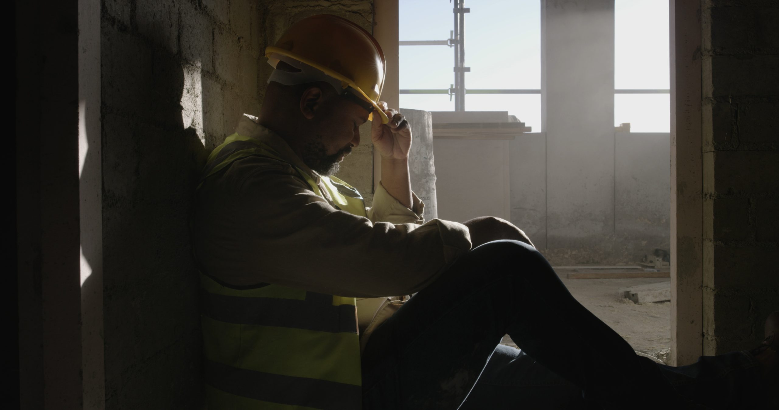 overworked tired safety professional sitting on ground with hard hat on needs safety support